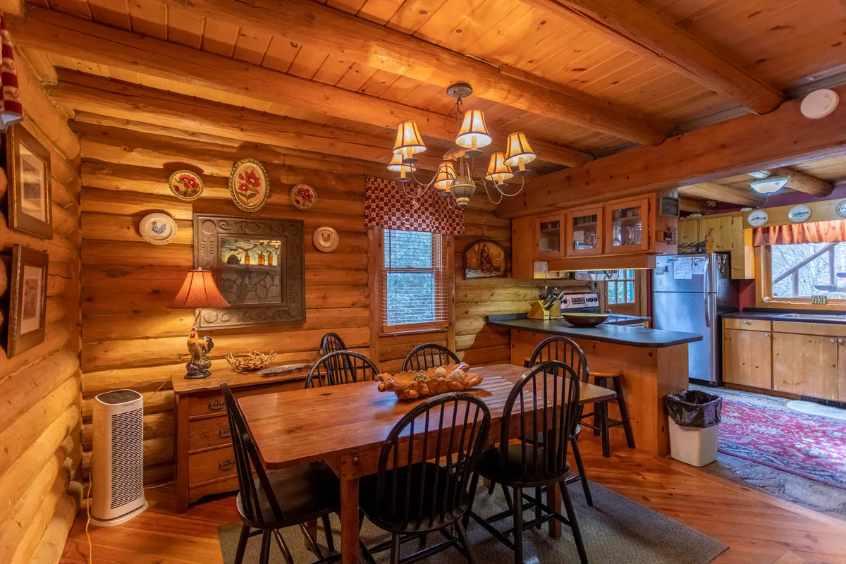 An elegant dining space with a wooden table, chandelier, decorative plates on the wall, and a lamp on a side table. The room radiates warmth and is set for gatherings, seamlessly connecting to nearby spaces—ideal for family dinners or group breakfasts after cooking in the kitchen.