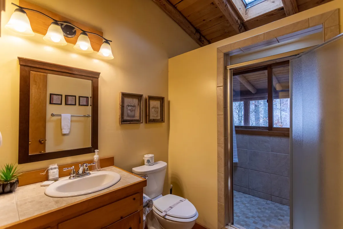 A calm, refreshing bathroom featuring a modern sink and vanity, shower area, and a well-lit mirror. Morning light pours in, suggesting the presence of a skylight. The mood is spa-like, clean, and inviting—perfect for relaxation and self-care.