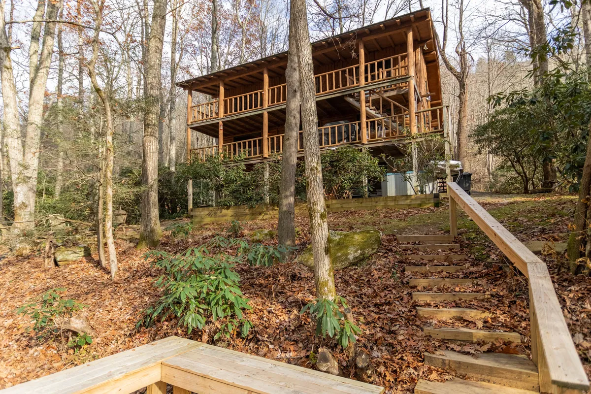 A wide view of the wooden cabin's exterior, surrounded by trees, with a staircase leading up to the inviting porch. The area is spacious and perfect for families or groups to gather, enjoy nature, and let kids explore safely.